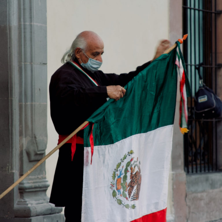 A man impersonating Miguel Hidalgo holding a flag of Mexico